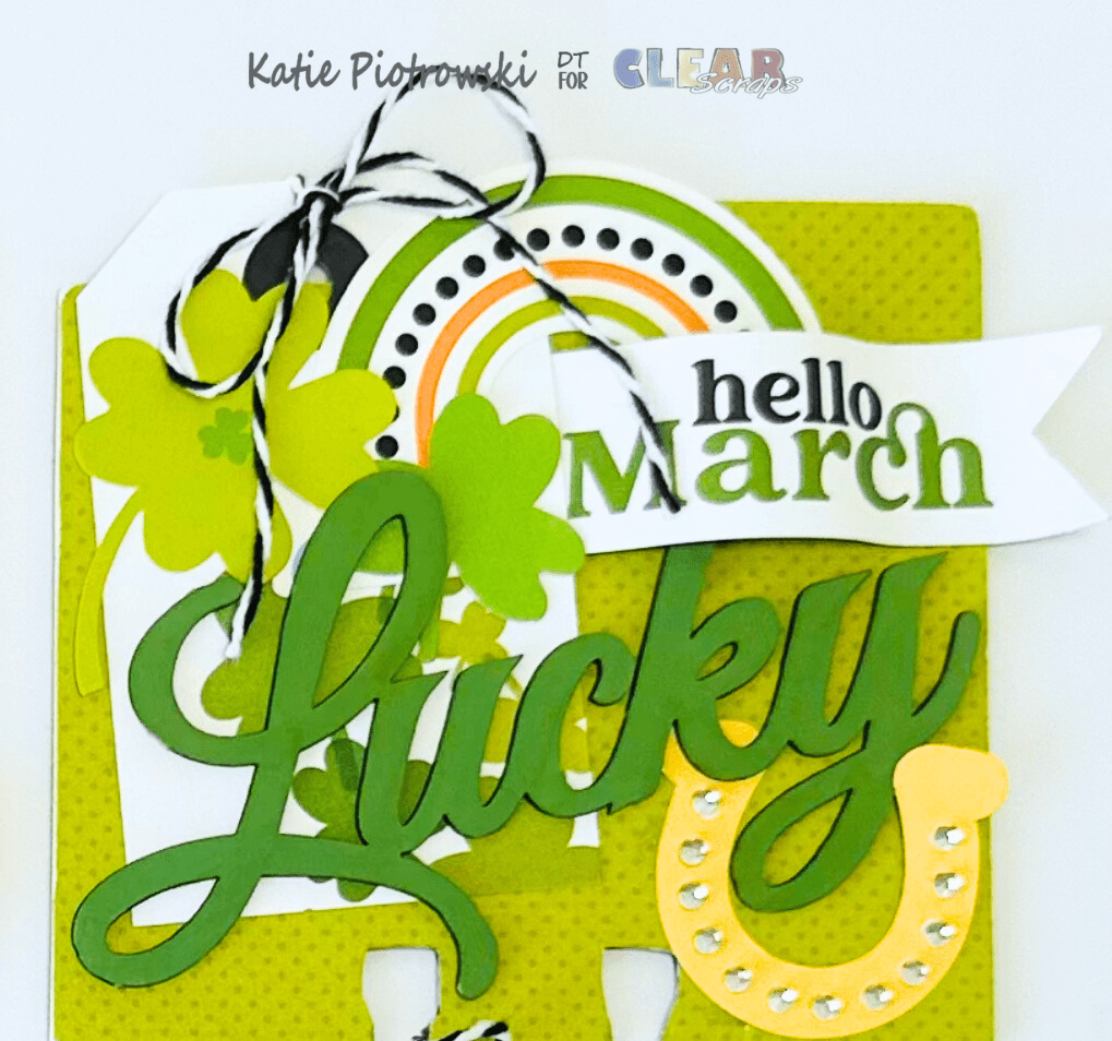 A decorative card for March featuring the word 'Lucky', clovers, a rainbow, and the phrase 'hello March'. The card has a vibrant green color scheme with layers and embellishments.