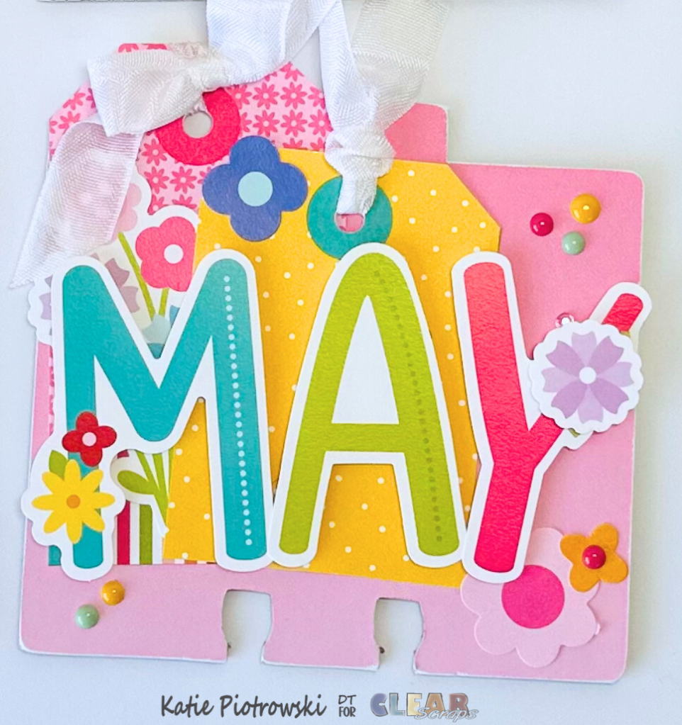 A colorful scrapbook tag for the month of May, featuring large, vibrant letters spelling 'MAY' alongside floral embellishments and decorative patterns.
