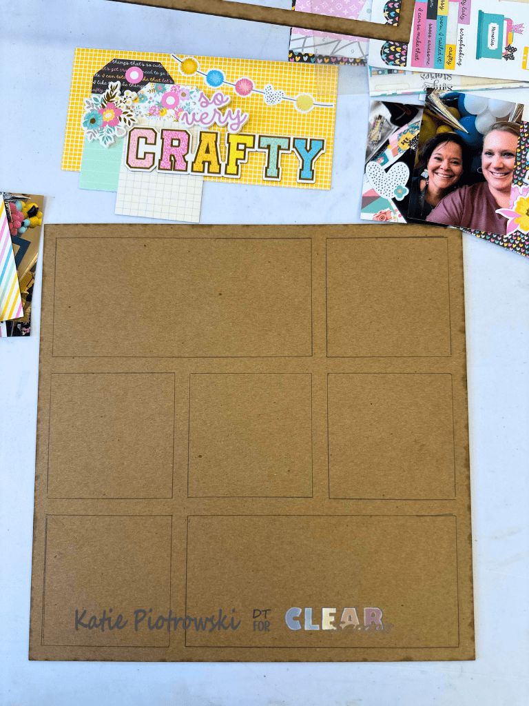 An arrangement of scrapbooking materials featuring a kraft paper layout with empty photo slots, decorative paper with the phrase 'so very CRAFTY,' and some floral stickers. There are also personal photos and colorful paper scraps nearby.